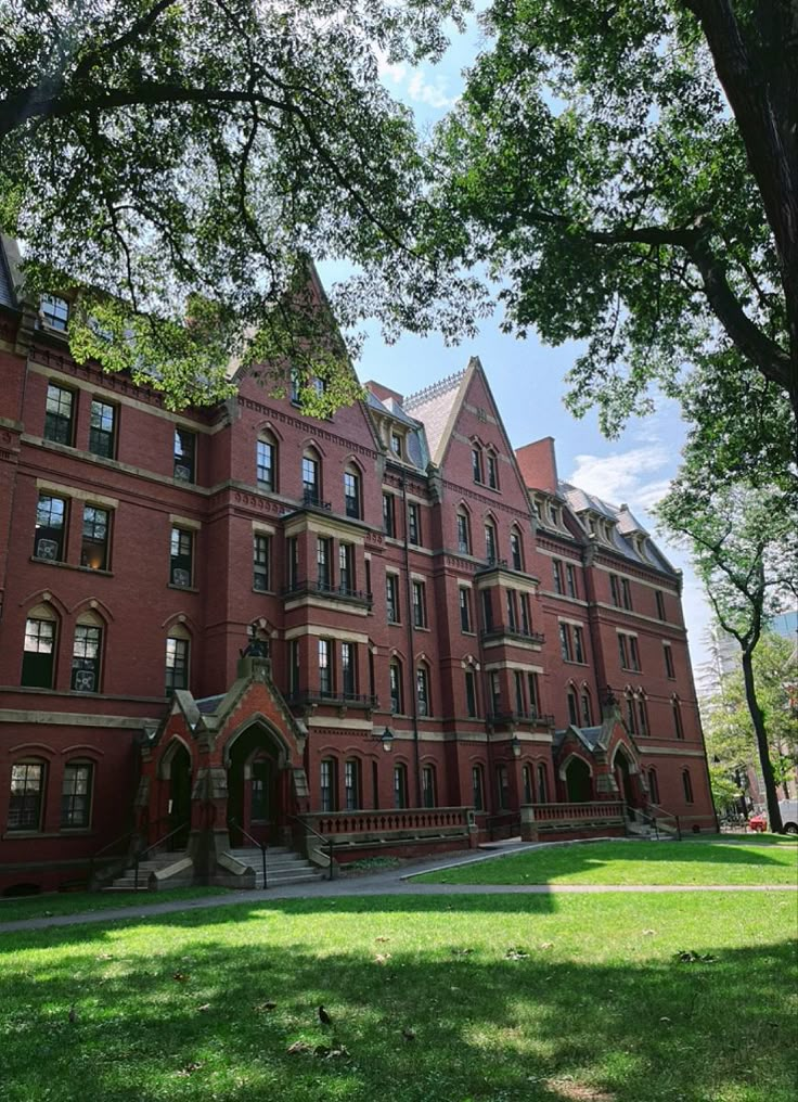 an old red brick building with many windows on the front and side, surrounded by trees