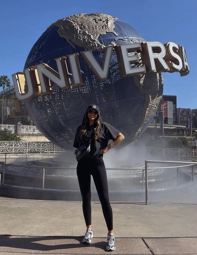 a woman standing in front of the universal studios sign with her hands on her hips