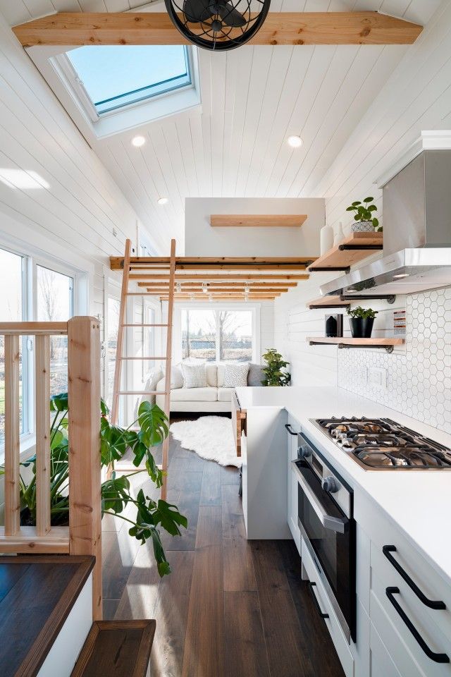 an open kitchen and living room area in a tiny home with white walls, wood flooring and ceiling beams