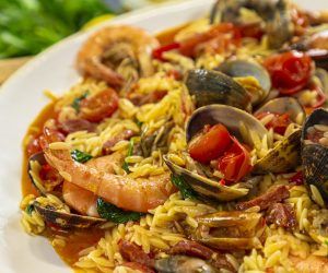 a white plate topped with rice covered in shrimp and clams on top of tomato sauce