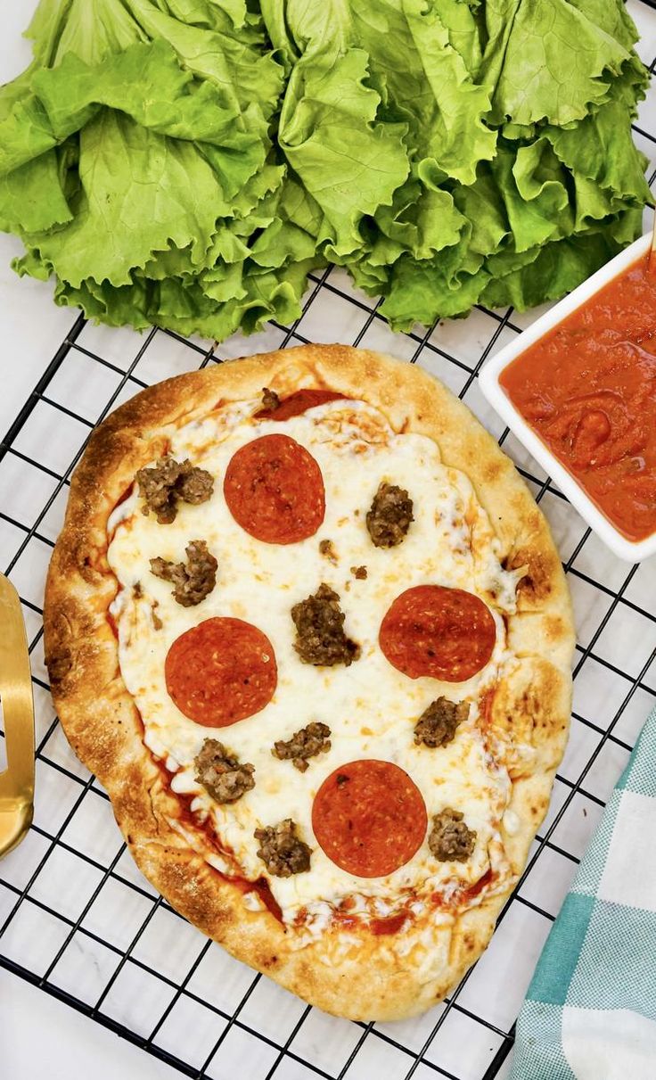 a pizza sitting on top of a cooling rack next to lettuce and sauce