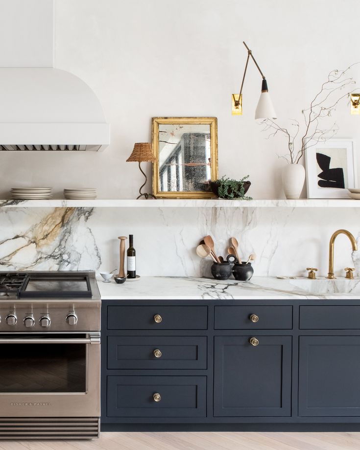 a kitchen with marble counter tops and blue cabinets, gold accents on the shelves above