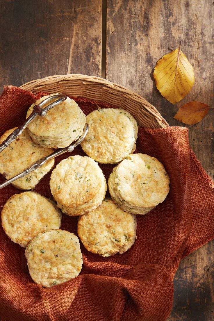 some biscuits are in a basket on a table with a spoon and orange napkin next to it