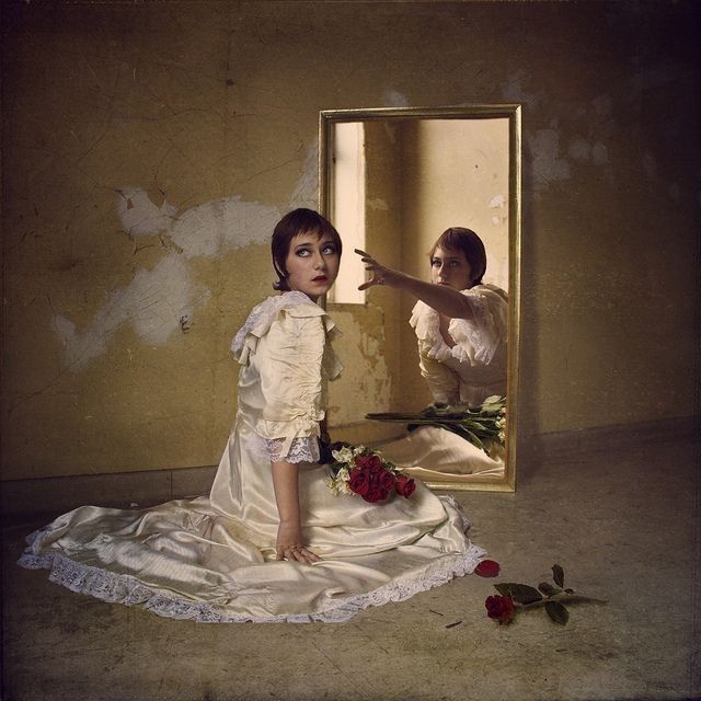 a woman in a white dress looking at herself in a mirror with roses on the floor