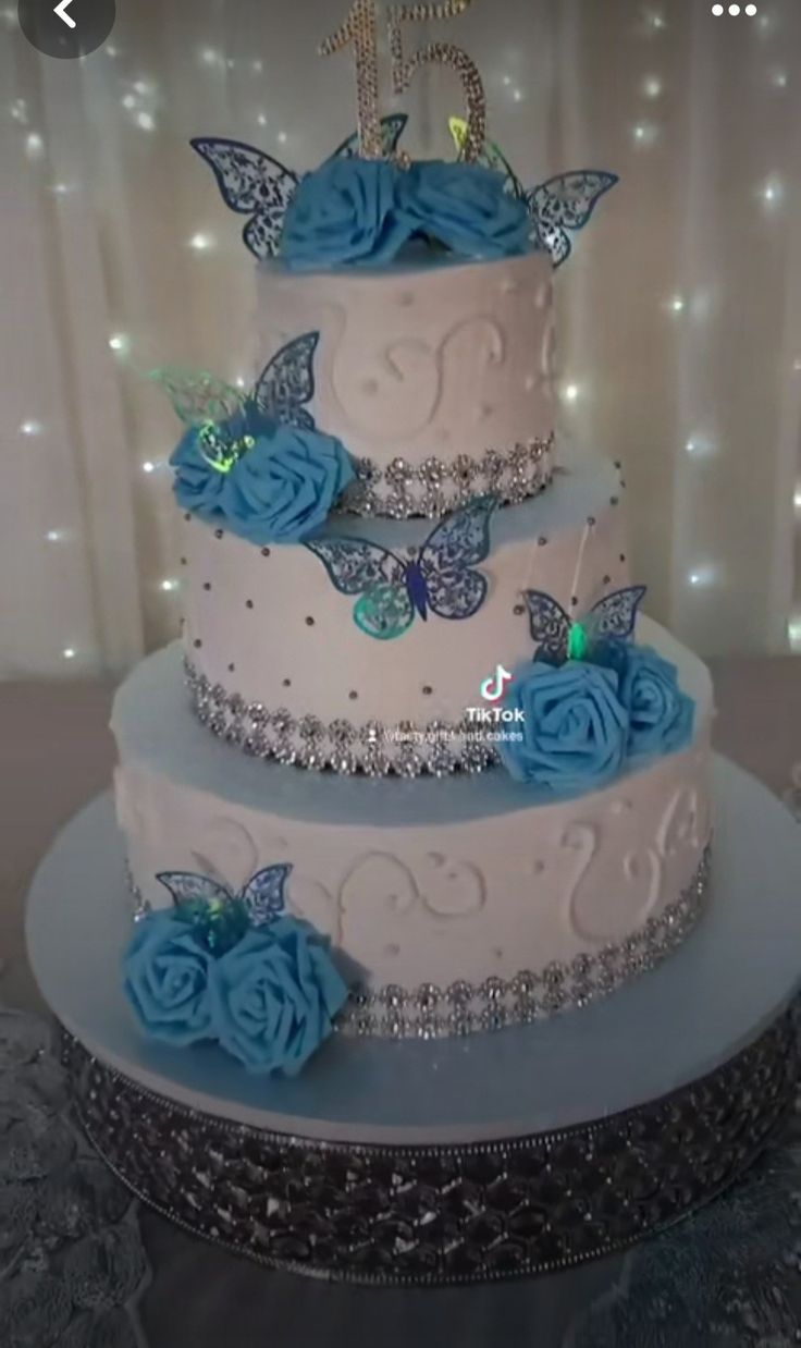 a three tiered cake with blue flowers and butterflies on it's side, sitting on a table