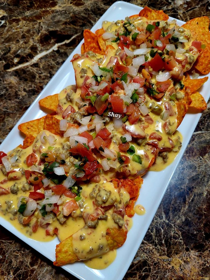 nachos with cheese sauce and toppings on a white plate next to tortilla chips