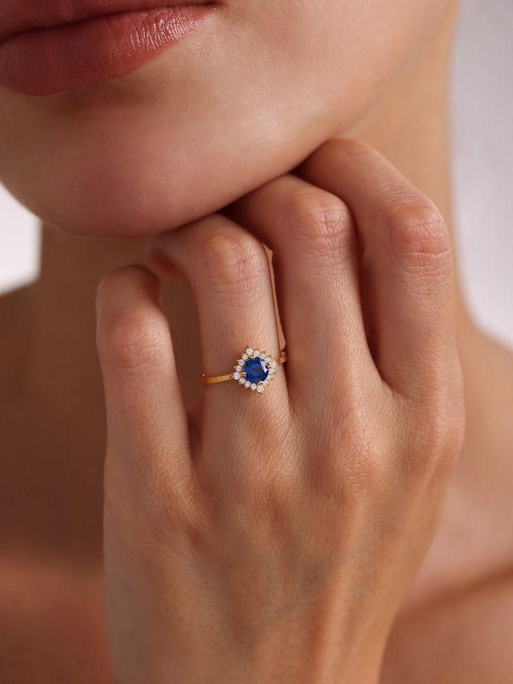 Your Blue Sapphire Engagement Ring is stylish, dainty and pretty ideal for everyday use. Details of solid gold handmade Dainty Sapphire Halo Ring are very eye-catching. It is a great gift for your loved ones. This jewelry will be an indispensable piece of yours. This meaningful Blue Gemstone Ring with high quality handwork will be a legacy you can leave to your family its.  * Sapphire and Diamond Ring Details * Material / Gold Kt:  14K (585), 18K (750), 8K (333) * Available Gold Colors: Yellow Gold, White Gold, Rose Gold * Top Width: 9.90 mm * Band Width: 1.95 mm * Band Thickness: 1.10 mm * The width may differ slightly due to handwork. * Gemstone: AAA Grade Sapphire and Cz Diamond * ABOUT PRODUCT Products with stones will be ready for dispatch within 3-5 business days, products without st Blue Open Ring Crystal Birthstone, Blue Birthstone Crystal Open Ring, Elegant Blue Diamond Ring For Proposal, Dainty Sapphire Ring With Center Stone, Blue Birthstone Crystal Ring, Delicate Blue Birthstone Jewelry, Fine Jewelry Blue Open Diamond Ring, Gold Sapphire Ring For Proposal, Sapphire Round Cut Jewelry For Proposal