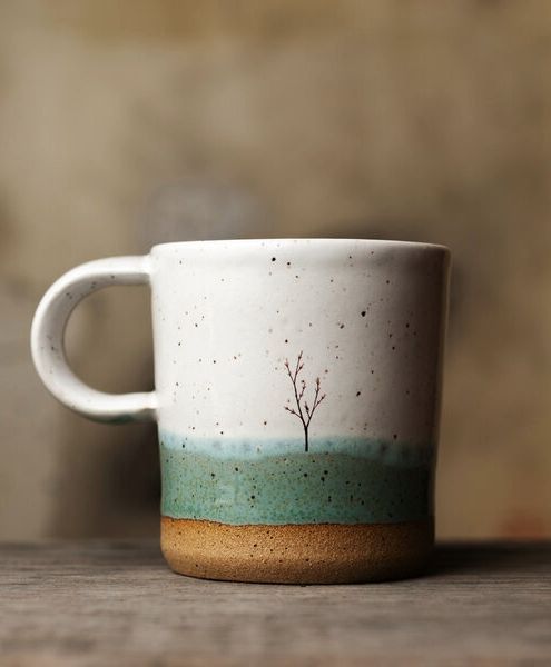 a white and green coffee cup sitting on top of a wooden table next to a wall