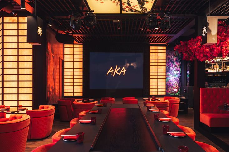 an empty restaurant with red chairs and black table cloths on the tables, in front of a screen that says aka