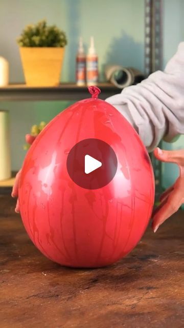 a person holding a large red ball on top of a wooden table