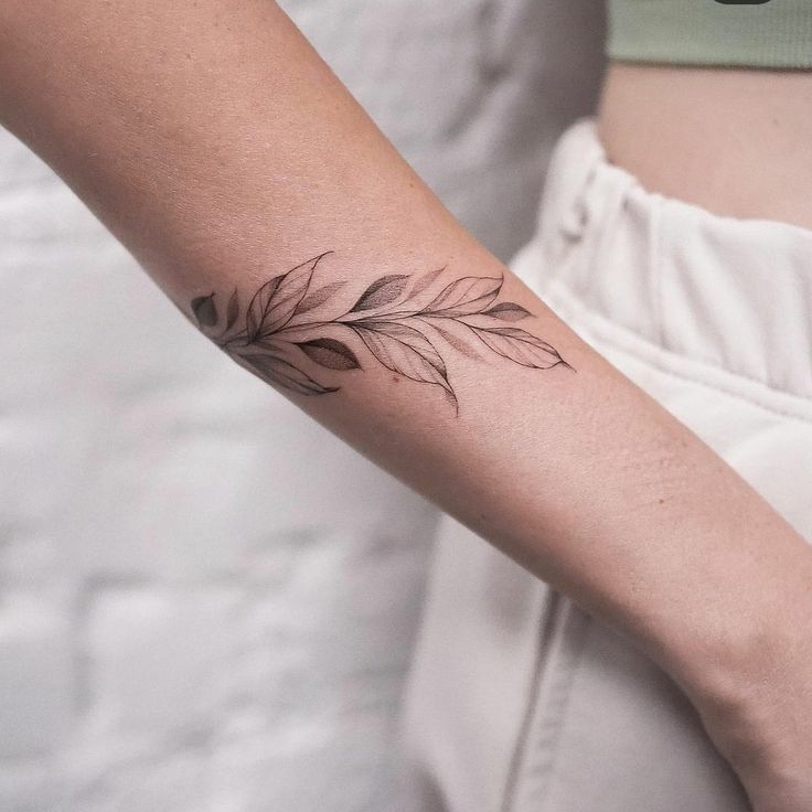 a woman's arm with a tattoo on it that has a branch and leaves