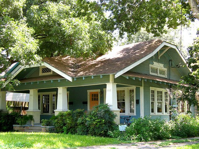 a green and white house sitting in the middle of a lush green yard with lots of trees