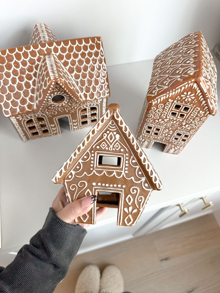 a person is holding up three gingerbread house shaped houses with holes in the roof