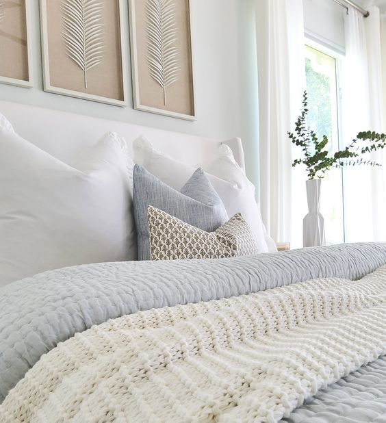 a bed with white sheets and pillows in front of two framed pictures on the wall