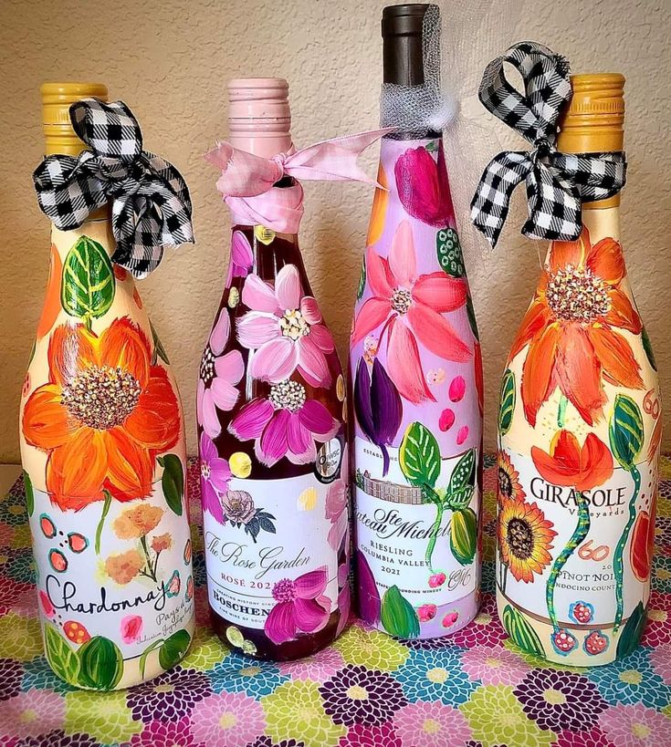 three bottles with flowers painted on them are sitting on a colorful tablecloth and one has a bow