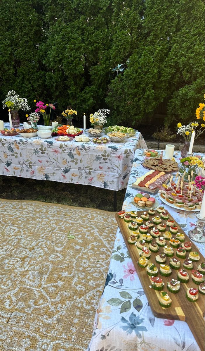 a table covered with cupcakes and pastries in front of some green trees