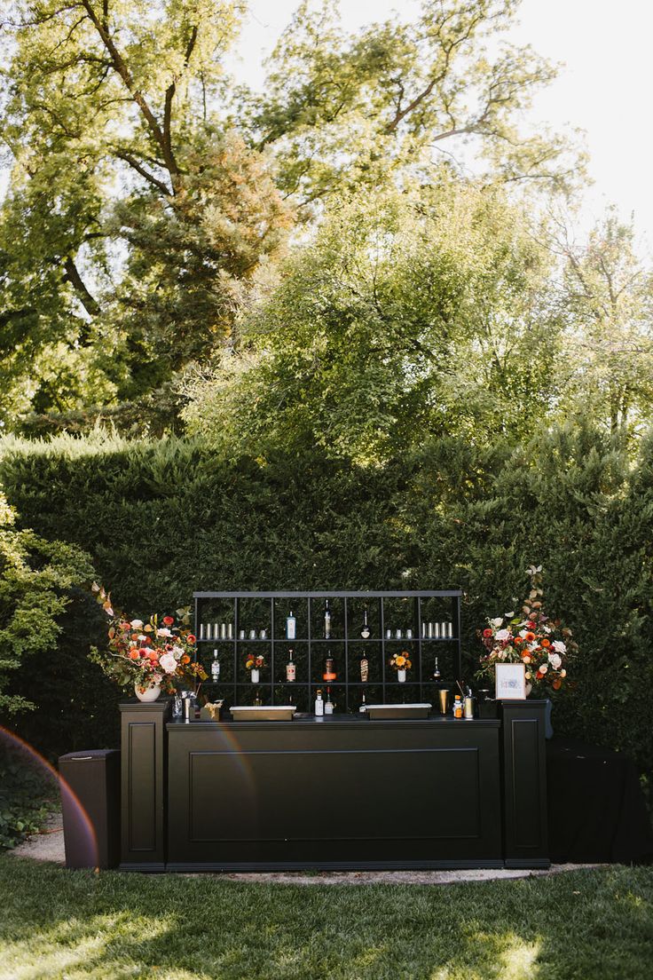 an outdoor bar set up in the middle of a yard with flowers and bottles on it