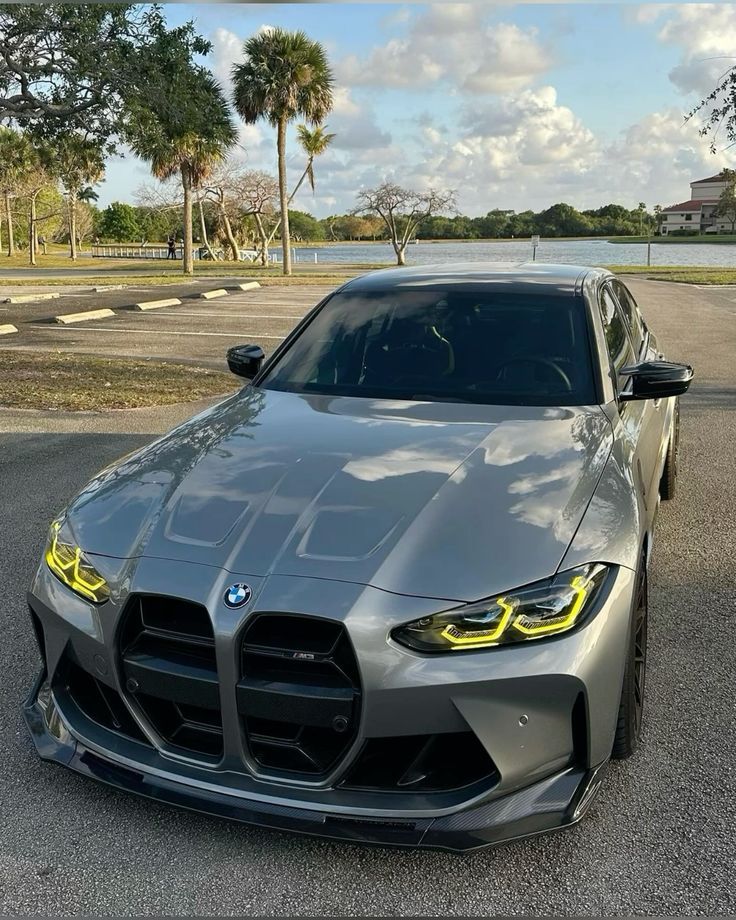 the front end of a silver sports car parked in a parking lot next to water