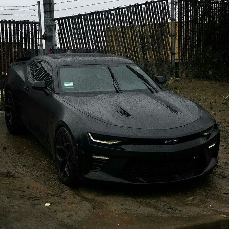 a black sports car is parked in the mud next to a fence and barbed wire