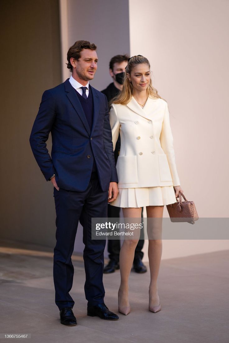 a man and woman standing next to each other in front of a building with people looking on