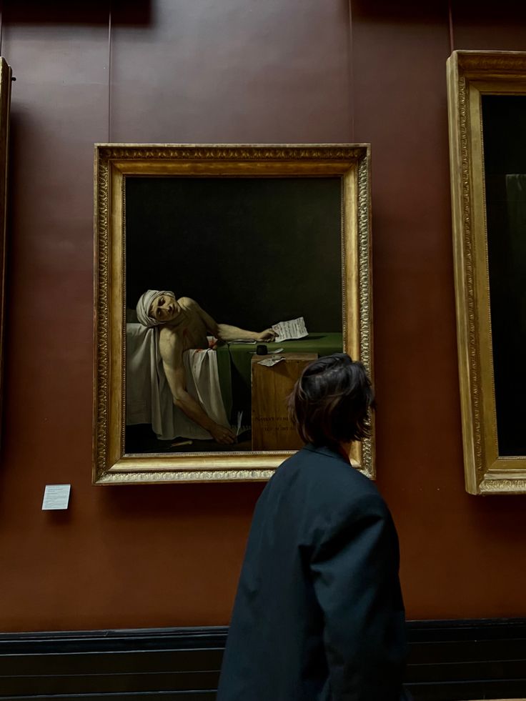 a woman looking at paintings on display in a museum