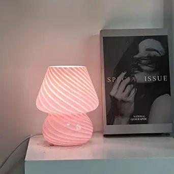 a pink lamp sitting on top of a white shelf next to a book and a poster