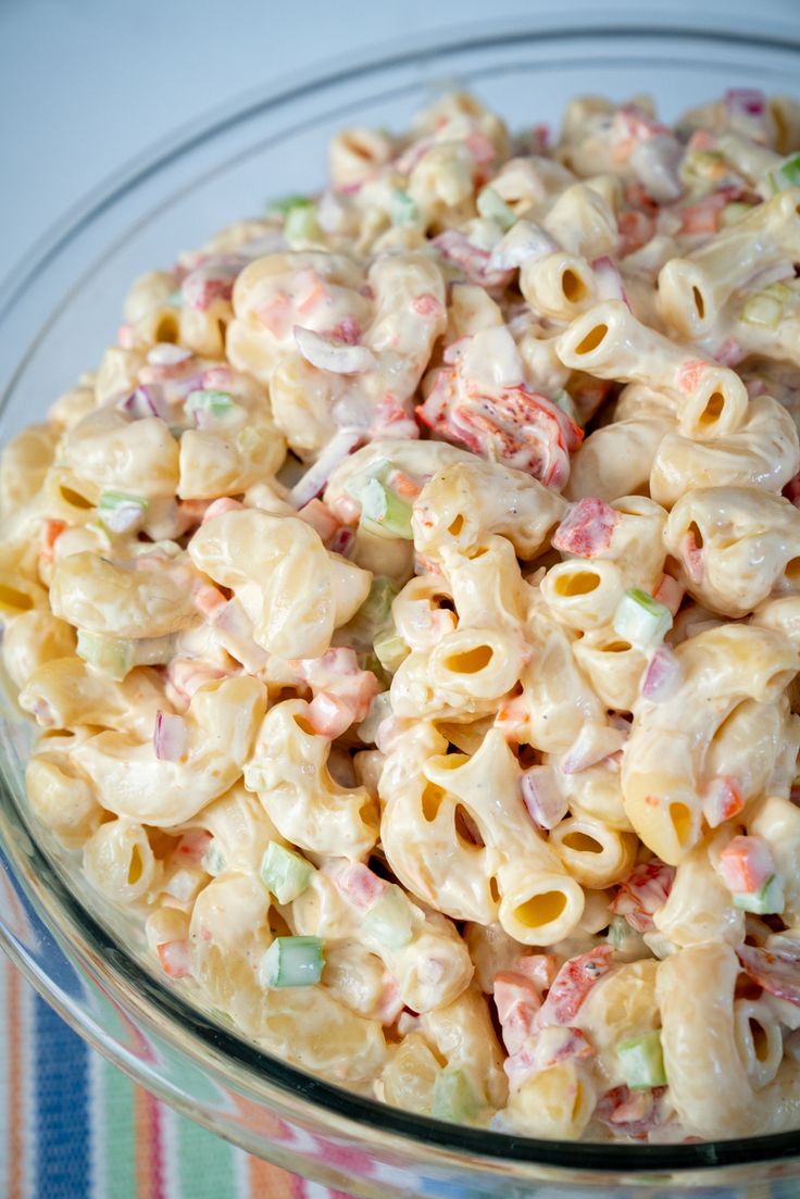 a glass bowl filled with macaroni salad on top of a striped table cloth