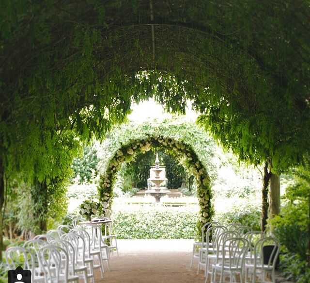 an outdoor wedding venue with white chairs and greenery on the walls, set up for a ceremony