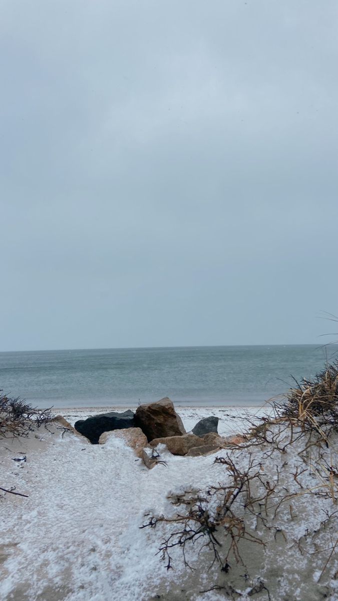 the beach is covered in snow and ice as it sits next to the ocean on an overcast day