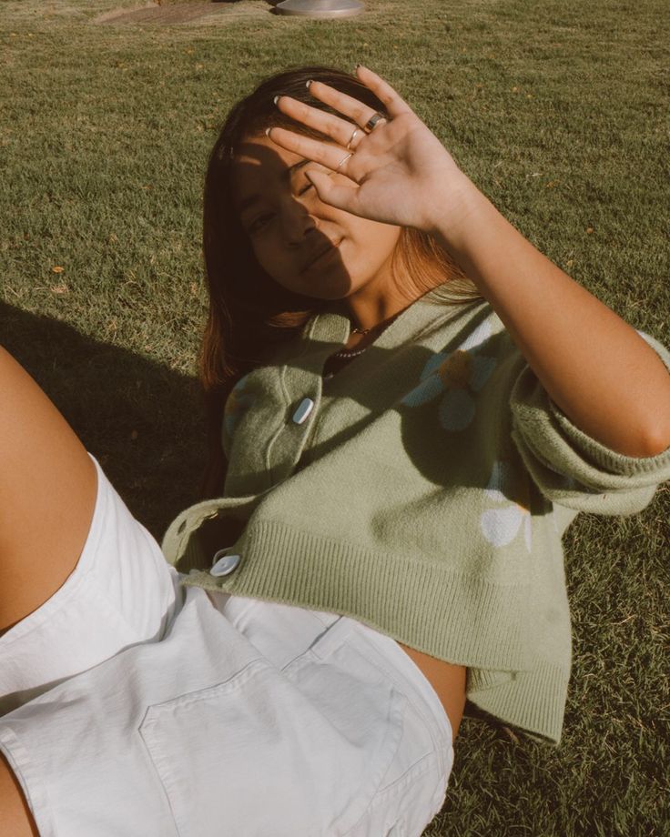 a woman laying in the grass covering her eyes