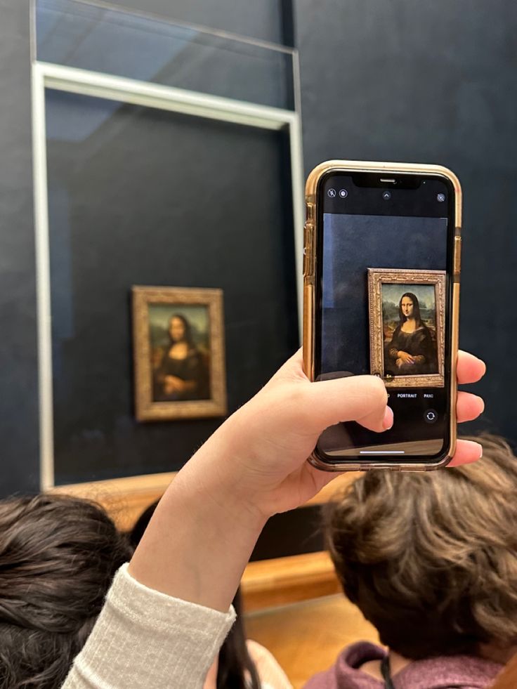 a person holding up a cell phone to take a selfie with the monaine painting in the background