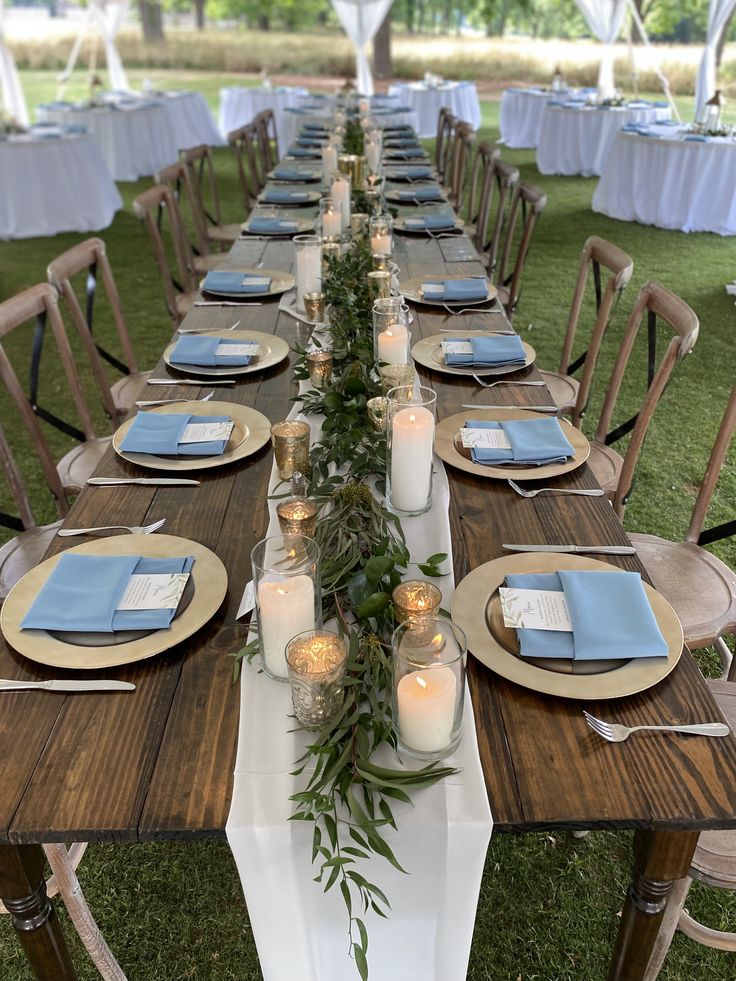 a long table is set with candles and place settings for an outdoor dinner party in the grass