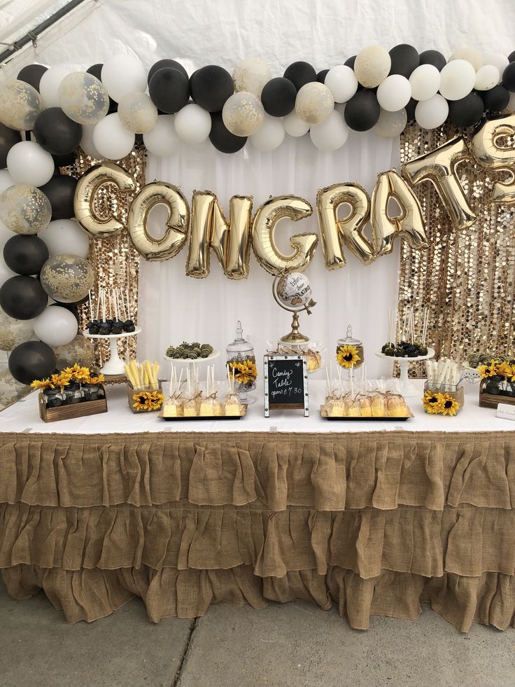 a table with balloons, sunflowers and confetti on it in front of a sign that says congrat