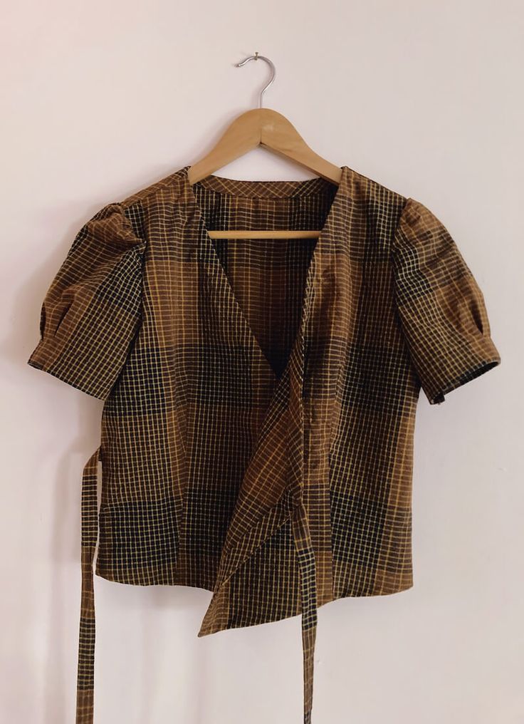 a brown and black checkered shirt hanging on a hanger next to a white wall