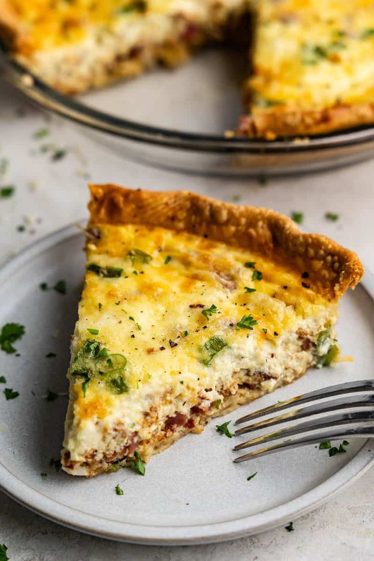 a slice of quiche on a plate with a fork next to the rest of the pie