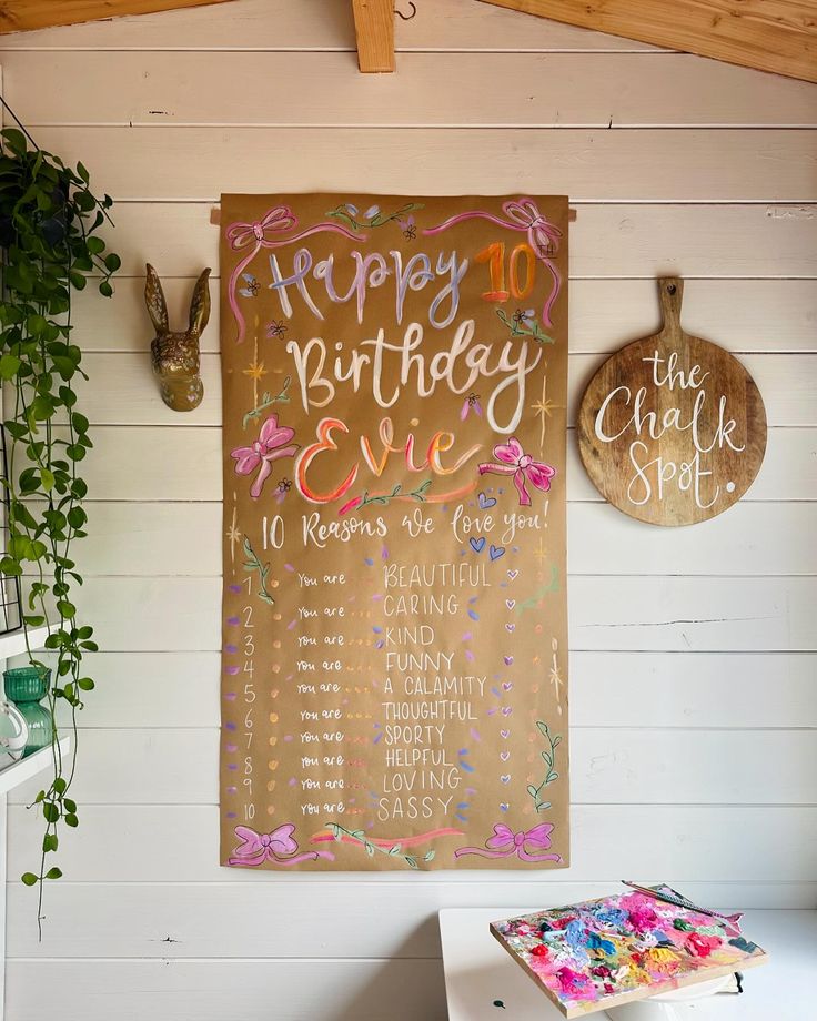 a birthday party sign hanging on the wall next to a potted plant and other decorations