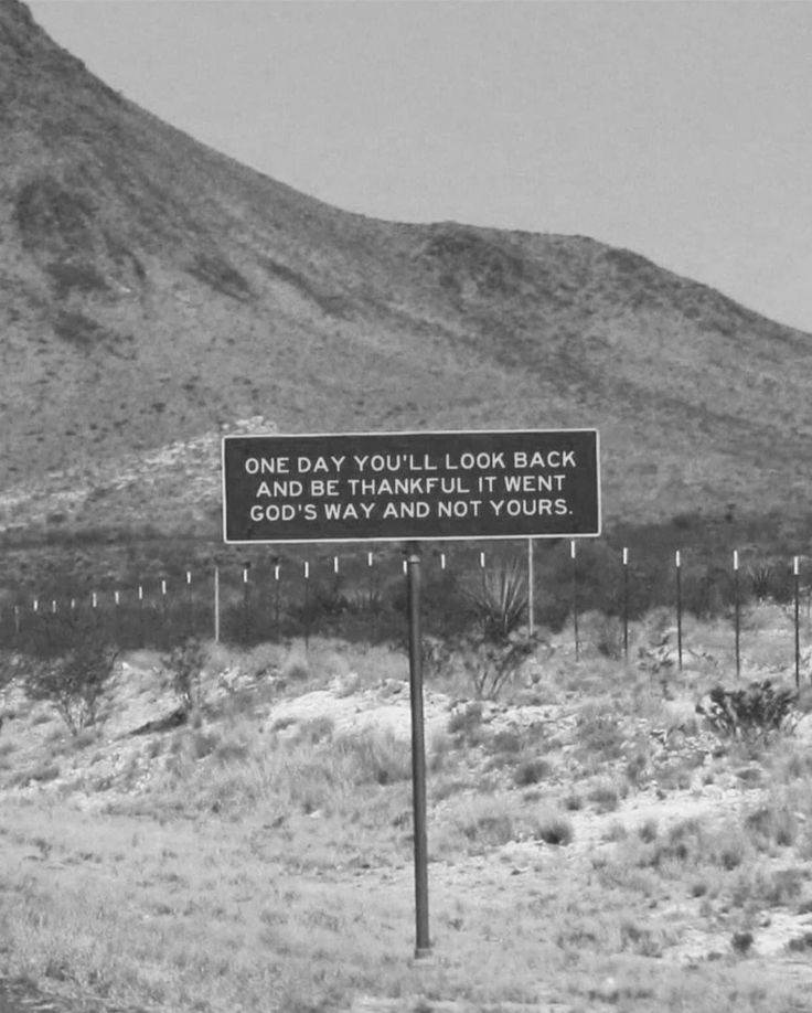 a black and white photo of a sign in the middle of nowhere with mountains in the background