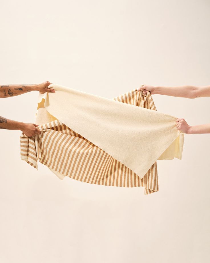 two hands holding up a white and brown striped towel with one person's arm in the air