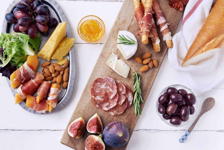 an assortment of meats and cheeses on a cutting board next to other foods