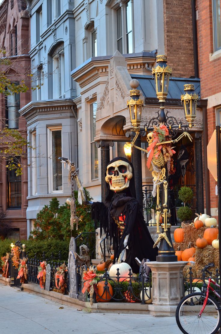 a street with halloween decorations and pumpkins on the sidewalk, including a skeleton statue