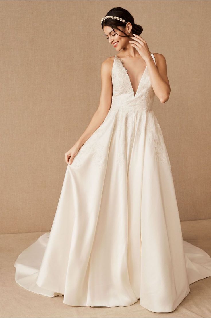 a woman in a white wedding dress standing next to a beige wall with her hand on her hair