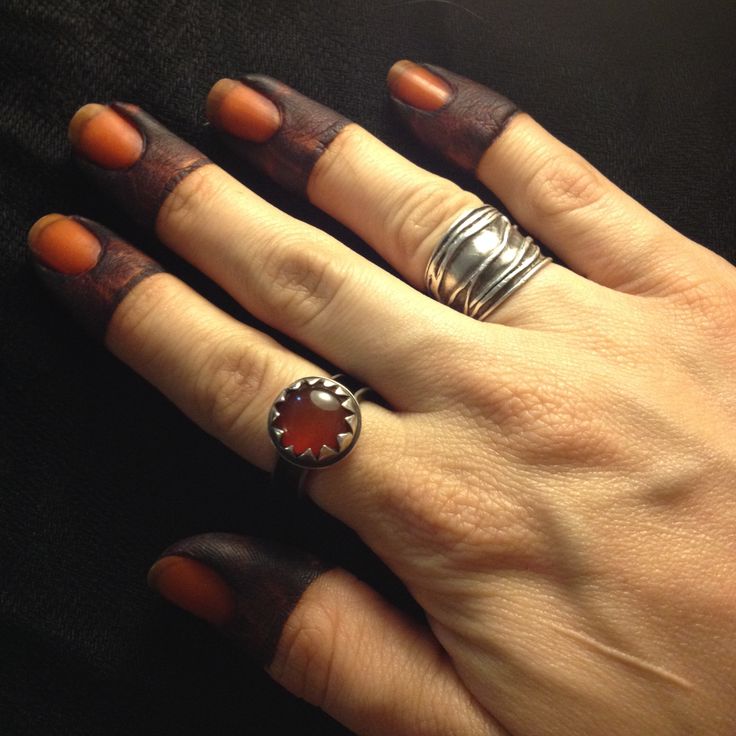 a woman's hand with two rings and an orange manicure on her fingers