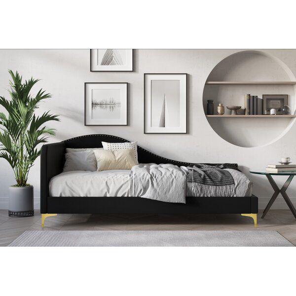 a black daybed sitting in front of a wall with pictures on it and a potted plant