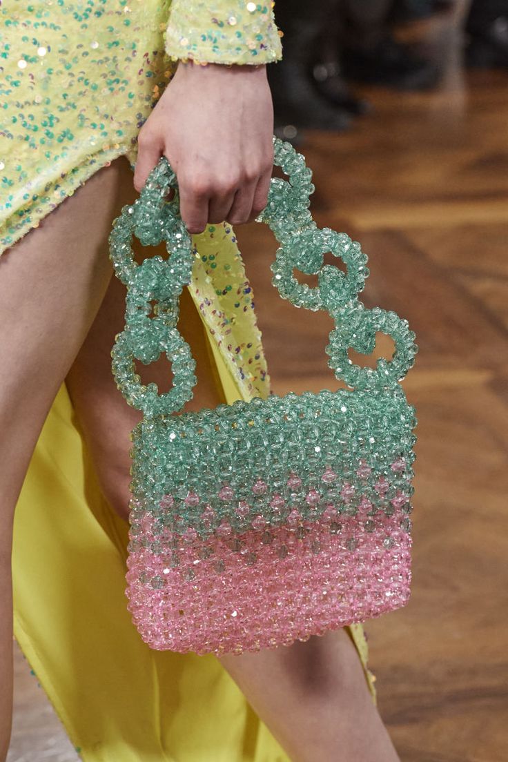 a woman's hand holding a pink and green beaded purse on top of a wooden floor