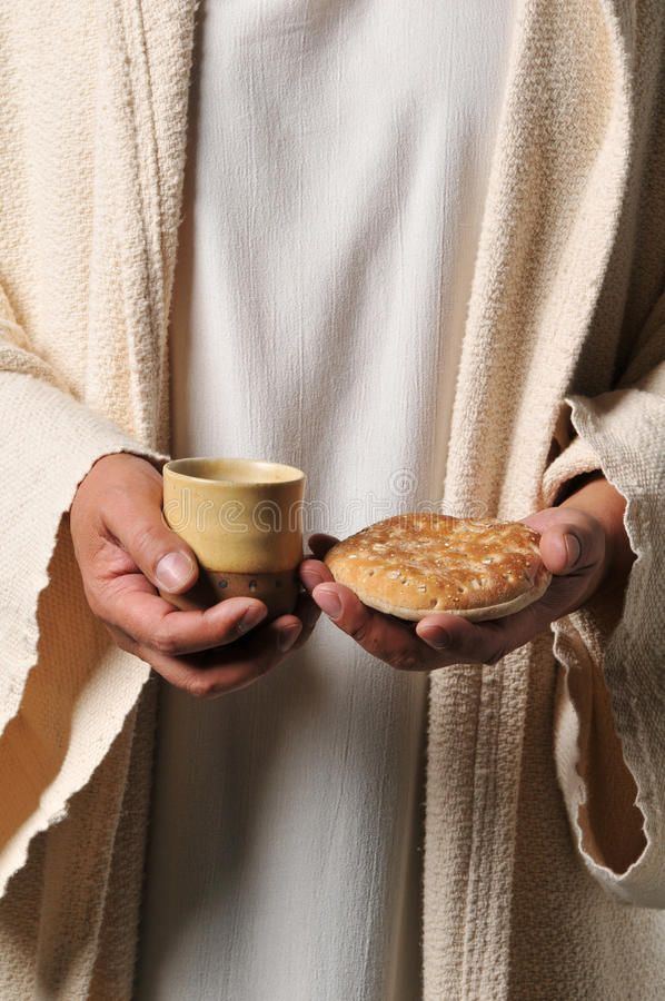 a man holding a cup and bread in his hands while wearing a white robe,