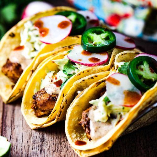 several tacos are lined up on a wooden table with green peppers and other toppings