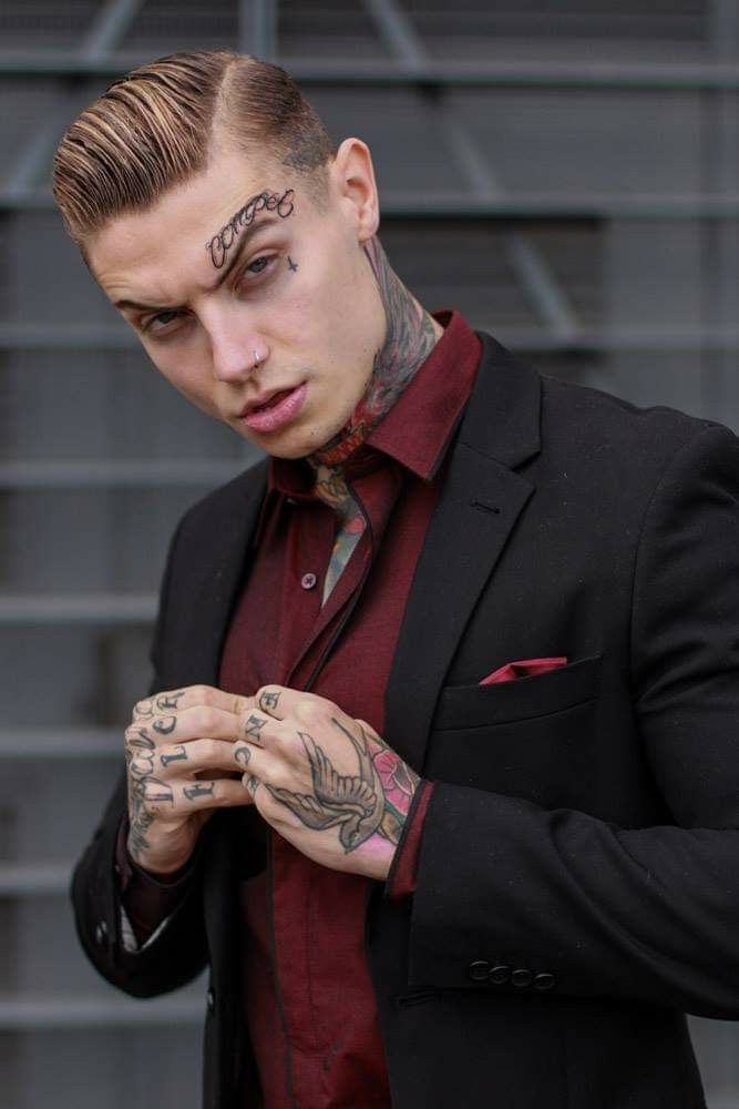 a man with tattoos on his face and chest standing in front of some stairs wearing a suit