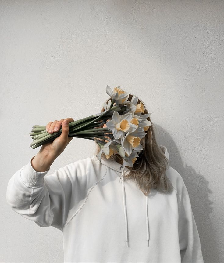 a woman in a white hoodie holding flowers up to her face