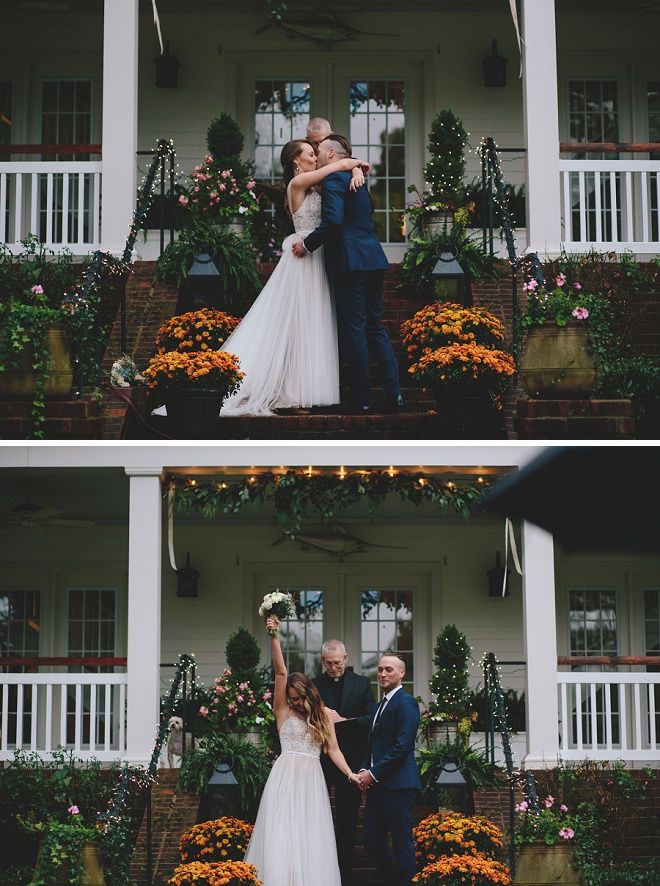 a bride and groom standing in front of a house with their arms around each other