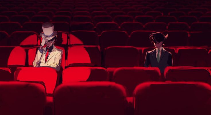 two people sitting in an empty theater with red seats